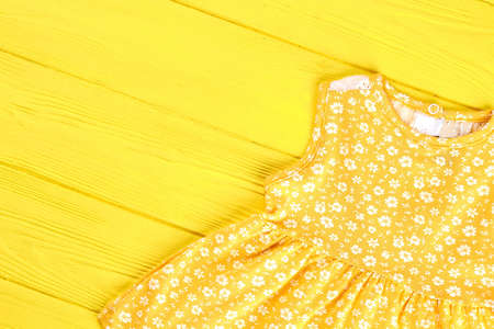 Infant girl vintage print dress. Baby-girl yellow floral print dress on yellow wooden background. Kids summer casual outfit.の写真素材
