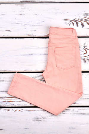 Girls new folded colored jeans. Solid peach color summer trousers for young women on old wooden background. Female denim clothes on sale.の写真素材