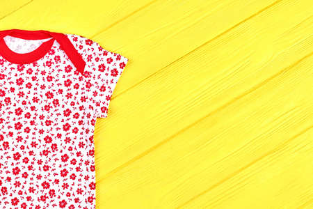 Baby girl white and red t-shirt. Infant girl new patterned summer bodysuit on yellow wooden background, copy space. Hot sale of infants summer apparel.の写真素材