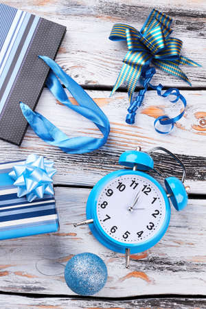 New Year ornaments and alarm clock. Blue gift box, Christmas ball, bow, shopping packet and alarm clock on old wooden background. Happy New Year.の写真素材