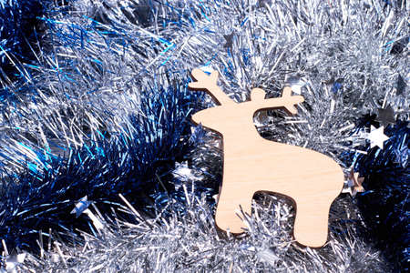 Cut out wooden deer on tinsels background. Shiny blue and silver Christmas garlands background and carved wooden silhouette of deer. Merry Christmas and happy New Year.の写真素材