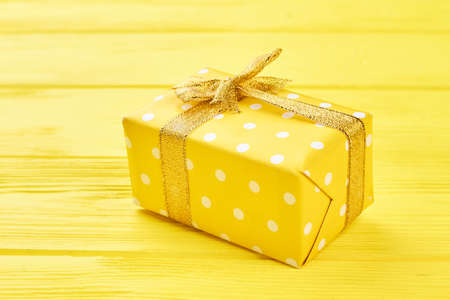 Yellow gift box on yellow background. Yellow dotted gift box tied with golden ribbon on yellow wooden background. Beautiful Christmas and New Year present.の写真素材