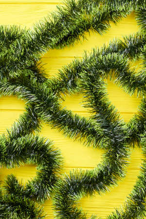 Green Christmas tinsels on wooden background. Christmas decorative garland of green color on yellow wooden background. New Year and Christmas concept.の写真素材