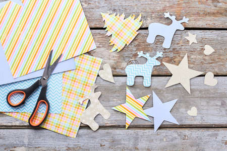 New Year paper silhouettes and scissors. Patterned paper, scissors and Christmas paper figures on old wooden background, top view. Christmas handmade paper ornaments.の写真素材