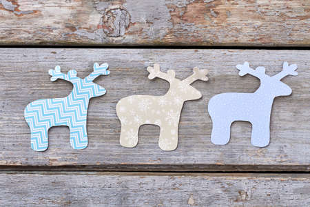 Three carved paper deers, wooden background. Cut out patterned paper deers on rustic wooden background. Winter handicraft decorations.の写真素材