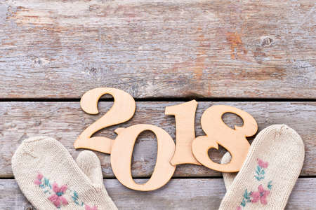 Cut out wooden number 2018 and gloves. Handmade wooden digit 2018 and white knitted mittens on old wooden background, copy space. New Year 2018 concept.の写真素材