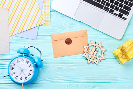 Laptop computer with Christmas decorations. Cropped computer, handmade envelope, gift box, cut out wooden decoration, alarm clock, gift box, decorative paper on blue wooden background, top view.の写真素材