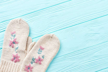 Pair of woolen mittens on wooden background. Female white knitted warm gloves on blue wooden...