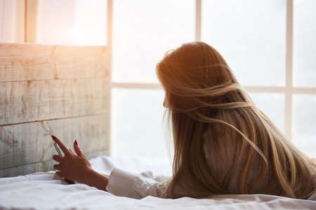 Woman in bed holding phone. Girl with smartphone.の写真素材