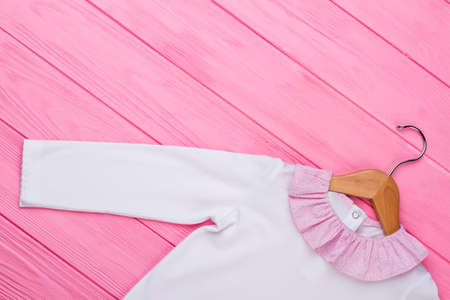 White shirt on wooden hanger. Beautiful garment with pink ruffle collar. Stylish kids clothing background.の写真素材