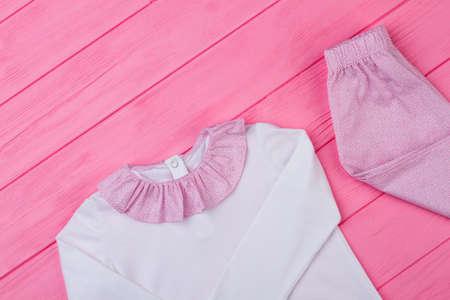 Pretty pajama set for little princess on pink wooden table, top view. T-shirt with ruffle collar and...