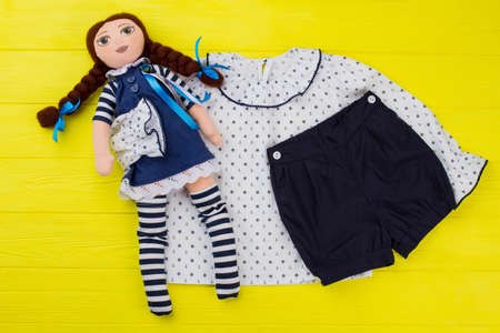 Girls toy and clothes on yellow table. Stuffed doll with ribbons. Sailor pajama set of top and shorts.の写真素材
