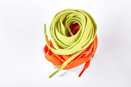 Stack of green and orange shoe laces. Colorful string for sport shoes over white background. Store...