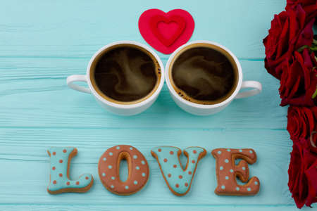 Valentines Day composition. Two coffee cups, red heart and letter cookies for Valentines Day. Roses buds and on blue background. Valentine Day idea.の写真素材