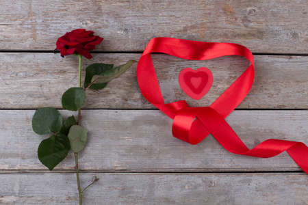 Beautiful red rose for Valentines Day. Composition of red rose and ribbon in heart shape on old wooden background. Love and romance.の写真素材