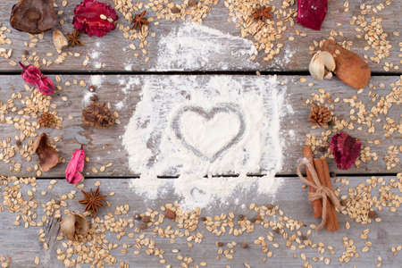 Heart painted on flour. Frame from oatmeal flakes, spices on old wooden background. Valentines Day composition on rustic wooden background. Healthy food concept.の写真素材