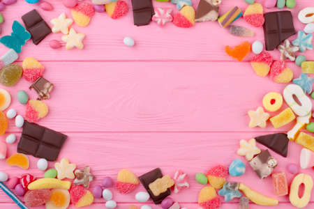 Frame from candies and copy space. Multicolored sweets on pink wooden background, space for text. Valentines Day greeting card.の写真素材