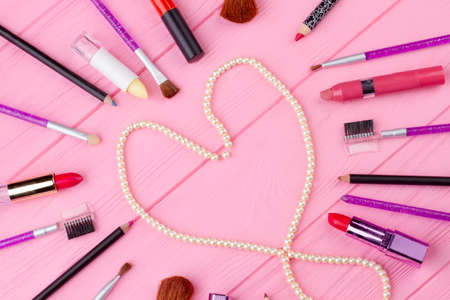 Makeup accessories collage, top view. Heart shaped white pearl necklace on wooden background. Cosmetics composition for Valentines Day.の写真素材