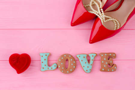 Word love from baked cookies. Red heart shaped velvet gift box and female leather shoes. Beautiful Saint Valentines Day composition on pink wooden background. Love and marriage concept.の写真素材