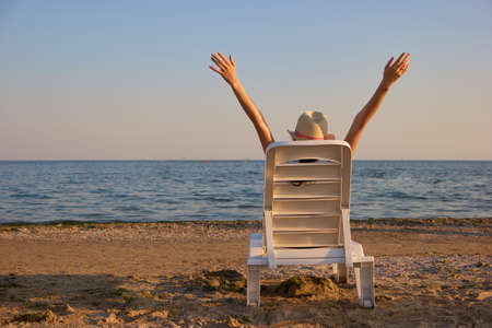 Backside view woman spread hands up on the beach. Perfect morning on the seashore.の写真素材