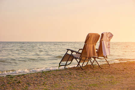 Deck chairs with towels on backrest on the seashore. Two empty deck chairs in romantic evening.の写真素材