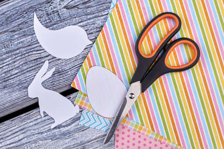 Patterned sheets of paper, scissors. Cut out paper figures of animals on wooden background. Easter handmade decor.の写真素材