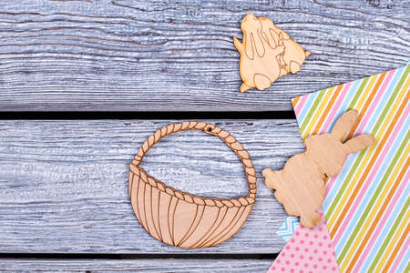 Easter cutwood figurines, top view. Cut out plywood basket, rabbits and patterned colorful sheets of paper on rustic wooden background. Handmade Easter ornaments.の写真素材
