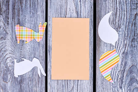 Blank card and paper animalistic silhouettes. Cut out paper birds and rabbits with empty paper card on rustic wooden background. Creative idea for easy Easter decorations.の写真素材
