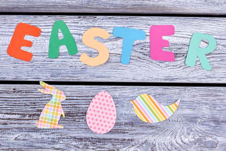 Easter colorful letters, wooden background. Inscription Easter and cut out paper figures of rabbit, bird and egg. Festive handcrafting for Easter holidays.の写真素材