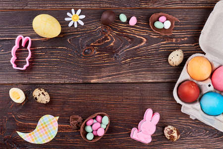 Easter composition on wooden background. Frame from sweets, quail and chicken eggs, rabbit molds,...