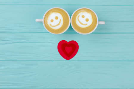 Valentines Day cappuccino, top view. Red heart and couple of cappuccino cups with smile on blue wooden background, top view. Valentines Day breakfast.の写真素材