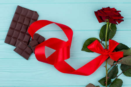 Fresh rose with red ribbon and chocolate. Red rose flower and chocolate on blue wooden background. Gift for Valentines Day.の写真素材
