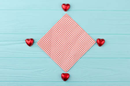 Heart shaped candies in red foil. Decoration with chocolate hearts and textile napkin on wooden background, top view. Valentines Day concept.の写真素材