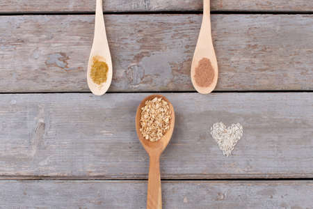 Spoons and cereals on wooden background. Oatmeal in wooden spoon. Heart shape from rice on rustic wooden background. Healthy food concept.の写真素材