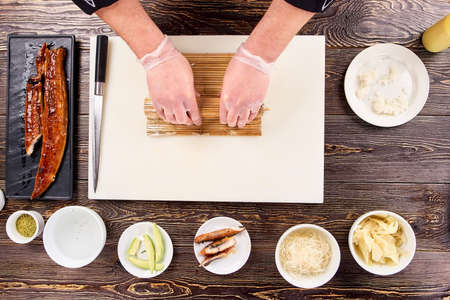 Food wrapping in sushi bamboo mat, top view. Rolling sushi on white board on kitchen table.の写真素材