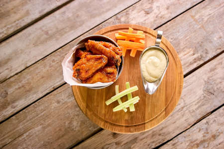 Hot and spicy chicken wings and sauce in pot. Fried chicken wings and side dish on round wooden board.の写真素材