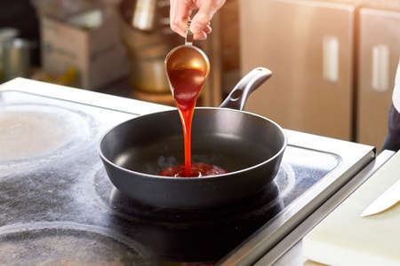 Tomato red sauce flowing onto pan. Hand pouring sauce from sauce boat onto pan.の写真素材