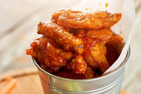 Juicy fried chicken meat pieces in sause, close up. Closeup hot chicken wings in aluminium bucket.の写真素材