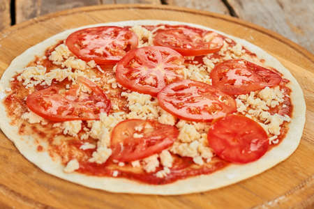 Unbaked tomato pizza. Juicy tomatoes on pizza. Tomato pizza ready to bake.の写真素材
