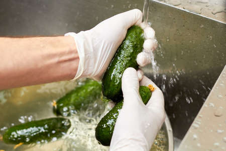 Rinsing cucumbers under tap water. Close up hands rinsing cucumbers.の写真素材