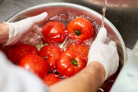 Washing big red tomatoes in bowl. Hands rinsing tomatoes in metal basin.の写真素材