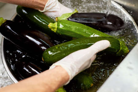 Chef hands rinsing vegetables under tap water, close up. Wet eggplant and courgettes washing under stream of water.の写真素材
