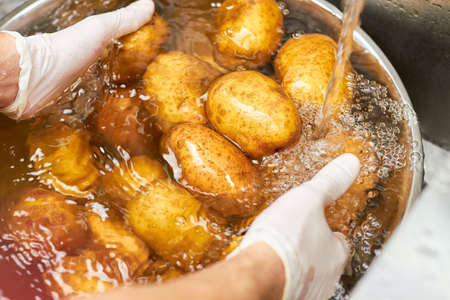 Washing potatoes piles under running water. Close up chef hands washing heap of potatoes in metal basin.の写真素材