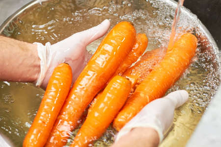 Chef hands washing heap of carrots under running water. Wet carrots rinsing under tap water.の写真素材