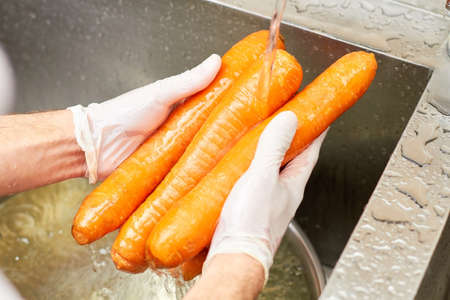 Four carrots washing at kitchen sink, close-up. Close up bench of carrots washing in a sink.の写真素材