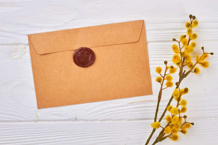 Handcrafted envelope on white wooden background. Pussy willow twig with flowering bud and craft envelope. Spring greeting idea.の写真素材