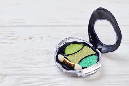 Eye shadows in round plastic box. Green light and dark eyeshadows on white wooden background. Eye make-up cosmetics.の写真素材