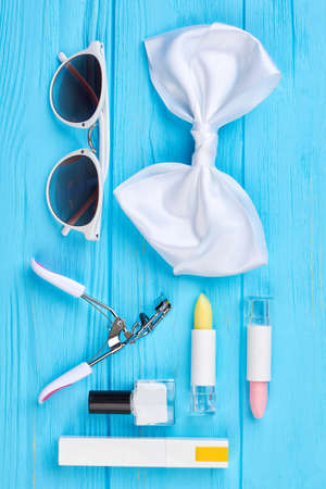Sunglasses, bow-tie and cosmetics. Decorative cosmetics and stylish accessories, blue wooden background. Beauty and fashion concept.の写真素材