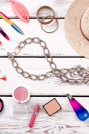 Woman fashion accessories, wooden background. Female stylish chain necklace, straw hat and cosmetics products. Women beauty essentials.の写真素材