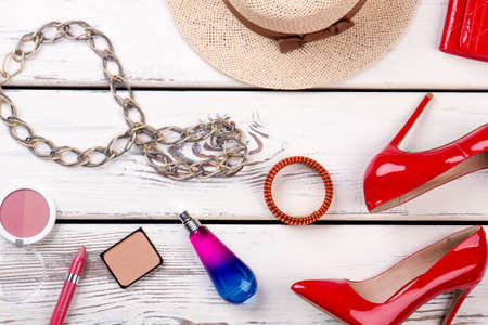 Beauty essentials on wooden background. Female red heels, straw hat and makeup accessories. Feminine beauty background.の写真素材